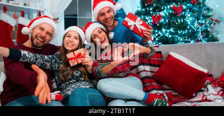 Aufregende und lustige Gruppe von Freunden in Weihnachtskleidung mit Neujahrsdekorationen im Hintergrund. Frohe Weihnachten und frohes neues Jahr Stockfoto