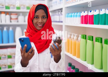 Junge schöne Frau Apotheker mit Smartphone hält Medikamentenflasche in der Apotheke Stockfoto