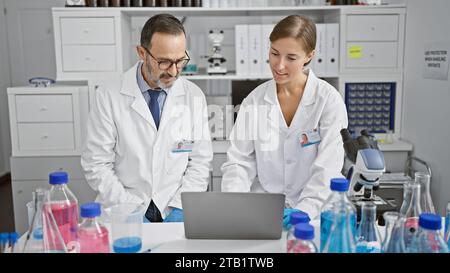 Zwei ernsthafte Wissenschaftler in Brille, vertieft in ein lebenswichtiges Forschungsgespräch über einen Laptop, die leidenschaftlich die neuesten medizinischen Erkenntnisse in ihrem sezieren Stockfoto