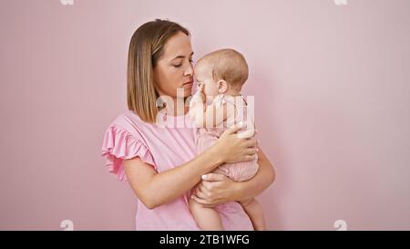 Entspannte Mutter umarmt und hält ihr Baby über einem kühlen, hübschen rosa isolierten Hintergrund und drückt ernsthafte Liebe in ihrem lässigen Lebensstil aus, strengthe Stockfoto