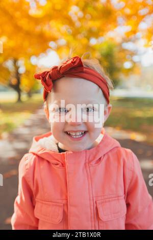 Kopfaufnahme von kleinen Mädchen, die mit rotem Stirnband lächeln, Herbsttag Stockfoto