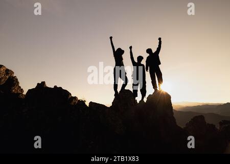 Glückliche Freunde Wanderer oder Touristen stehen mit erhobenen Armen auf der Bergspitze gegen Berge und blicken auf den Sonnenuntergang. Unabhängige Wanderreise, Erfolg. Stockfoto