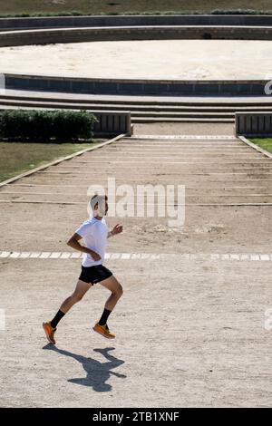 Seitenansicht eines fitten Mannes, der neben einem athletischen antiken Stadion läuft. Stockfoto