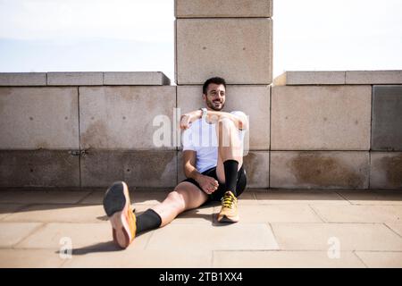 Junger glücklicher männlicher Laufsportler, der sich vom Training auf dem Boden erholt Stockfoto