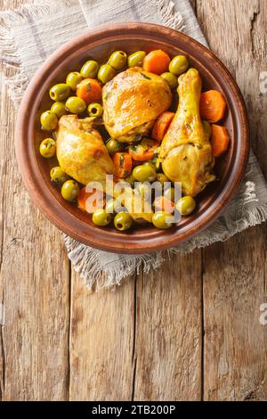 Traditionelles algerisches Essen Tajine Zitoune aus Hühnchen, Karotten und grünen Oliven in Nahaufnahme auf Holztisch. Vertikale Draufsicht von oben Stockfoto