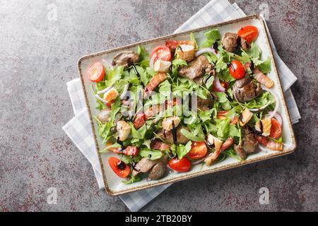Frischer Gemüsesalat mit gegrillter Hühnerleber und Speck in Nahaufnahme auf dem Teller auf dem Tisch. Horizontale Draufsicht von oben Stockfoto