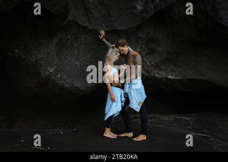 Junges, schönes Paar am schwarzen Sandstrand, Bali. Tätowierter Mann. Stockfoto
