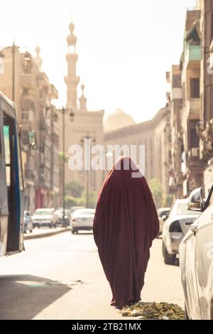 Eine muslimische Frau, die eine rote Burka trägt, läuft auf den Straßen von Kairo Stockfoto