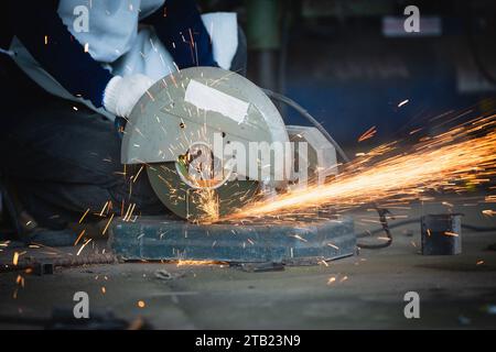 Innenraum der Maschinenfabrik für Schwerindustrie mit Industriearbeiter mit Winkelschleifer und Schneiden eines Metallrohrs. Schneiden von Metall und Stahl mit einem Kamm Stockfoto