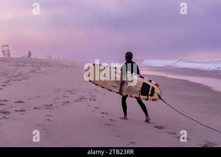 Ein älterer Surfer spaziert am Strand mit seinem Surfbrett auf Cape Cod Stockfoto