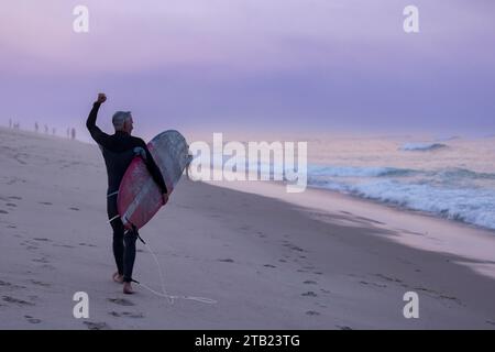 Ältere Surfer jubeln Surfer am Strand bei Sonnenuntergang auf Cape Cod an Stockfoto