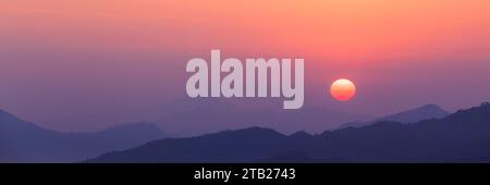 Mehrschichtige Bergsilhouetten bei Sonnenuntergang mit lebendigem Himmel Stockfoto