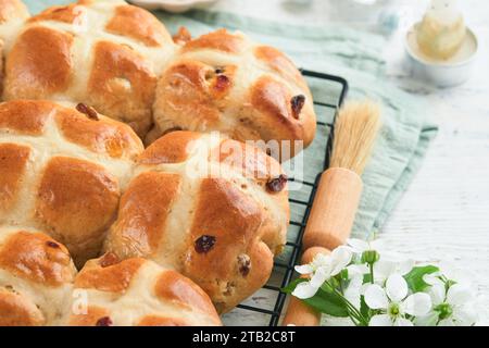 Ostern heiße Kreuzbrötchen. Traditionelle Osterspezialitäten sind Kreuzbrötchen mit Rosinen, Butter, Schokoladeneiern mit blühenden Kirschen oder Apfelblüten auf Rost Stockfoto