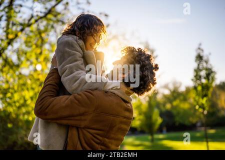 Porträt eines glücklichen Liebespaares im Park bei Sonnenuntergang. Der Mann hält seine Frau in Händen. Stockfoto