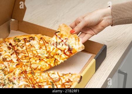 Die Hand der Frau nimmt ein Stück Pizza aus einer Schachtel. Pizza nach Hause geliefert. Köstliches Stück Pizza Stockfoto