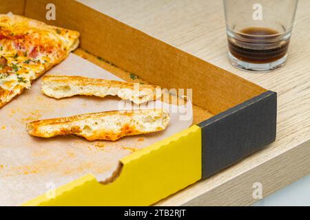 Trockene Pizzabandkruste liegt in einer Kiste. Trockene Pizzakruste. Übrig gebliebene Pizza auf dem Tisch Stockfoto
