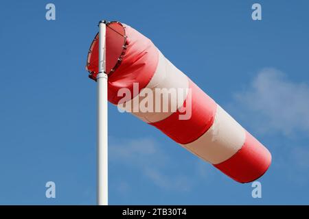 Eine rot-weiß gestreifte Windsocke an einer Stange vor einem blauen Himmel. Stockfoto