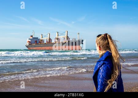 Ein weiblicher Tourist sieht ein großes Frachtschiff Blue Shark an, das vor der Küste des Schwarzen Meeres auf Grund gelaufen ist. Vitjasevo, Russland-02.12.2023 Stockfoto