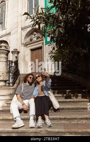 Ein wunderschönes Hipster-Paar, das verliebt ist, sitzt auf der alten Straße und macht Selfie am Telefon Stockfoto