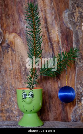 Zwei Tannenwedel mit einer einzelnen billigen hängenden Kugel saßen in einem Smiley Gesicht Eierbecher Konzept Budget Kosten für lebende Krisen weihnachtsbaum Dekoration Stockfoto