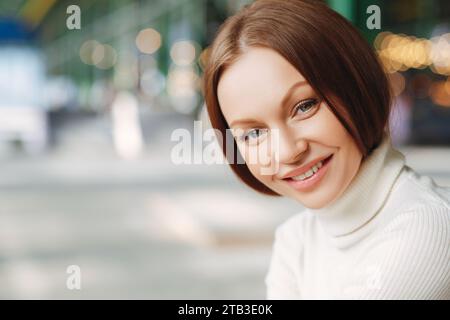 Lächelnde Frau in weißem Rollkragen mit urbanen Bokeh-Lichtern Stockfoto