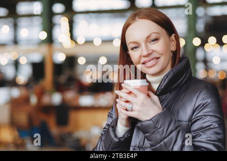 Lächelnde rothaarige Frau, die Kaffee in einem städtischen Café genießt Stockfoto