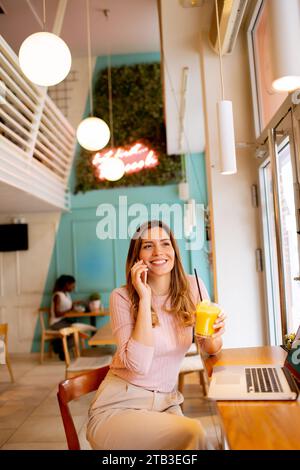 Eine junge Frau, die an einem Laptop arbeitet und im Café frischen Orangensaft trinkt Stockfoto