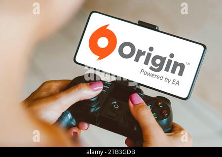 Brasilien. Dezember 2023. In dieser Fotoabbildung wird das Origin-Logo auf einem Smartphone-Bildschirm angezeigt, während eine Person auf einem Gaming-Gamepad spielt. Quelle: SOPA Images Limited/Alamy Live News Stockfoto