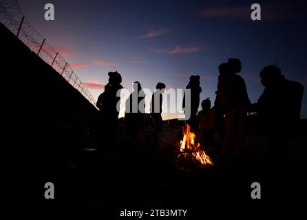 Jacumba Hot Springs, Kalifornien, USA. Dezember 2023. Eine Asylsuchende Migrantenfamilie mit kleinen Kindern aus Columbia versucht, sich neben einem Feuer in einem Freiluftlager an der Grenze zwischen den USA und Mexiko in der Nähe der kleinen Wüstengemeinde Jacumba Hot Springs im San Diego County warm zu halten. Hunderte von Asylbewerbern überqueren täglich die Grenze in die Vereinigten Staaten und erleben kalte Nächte, in denen sie auf ihre Bearbeitung warten. (Kreditbild: © K.C. Alfred/ZUMA Press Wire) NUR REDAKTIONELLE VERWENDUNG! Nicht für kommerzielle ZWECKE! Stockfoto