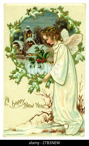 Original Edwardian Era Happy New Year Grußkarte eines Engels mit einem Haufen stechpalme und einer Kirche im Hintergrund in einer Winterlandschaft. Um 1905, 1910. GROSSBRITANNIEN Stockfoto