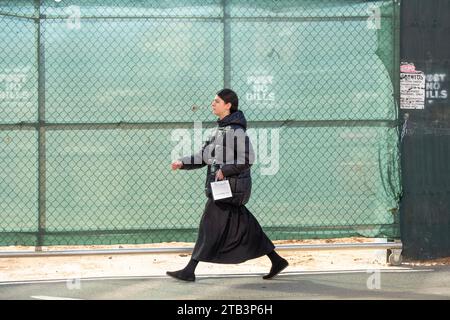 Ein bescheiden gekleidetes chassidisches Mädchen in einem langen Rock spaziert auf einer Baustelle in der Lee Avenue in Williamsburg, Brooklyn, New York. Stockfoto