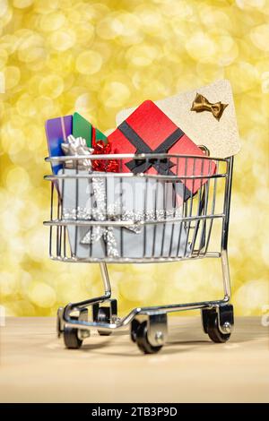 Ein Miniatur-Einkaufswagen voller Geschenkkarten gegen ein goldfarbenes Bokeh-Konzept für Online-Shopping Stockfoto