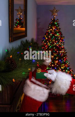 Der Weihnachtsmann legt 2 Geschenkkarten in einen Strumpf, der am Kaminsims hängt Stockfoto