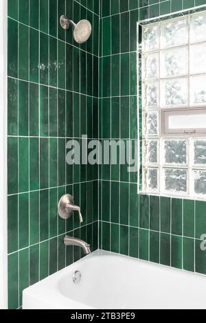 Das Badezimmer verfügt über eine Dusche mit leuchtend grünen vertikalen Glasfliesen, eine eingebaute Nische und ein Fenster mit Glasblöcken. Stockfoto