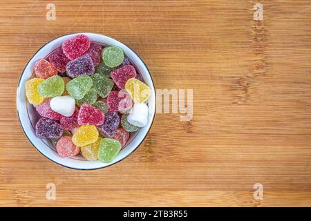 Bunte Fruchtbonbons, gummiartige Bonbons in einer Keramikschale auf einem hölzernen Schneidebrett. Blick von oben. Stockfoto