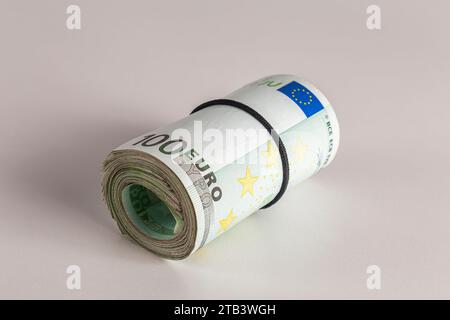 Eine Rolle von hundert Euro-Banknoten liegt auf einem Tisch vor hellem Hintergrund in der Nähe Stockfoto