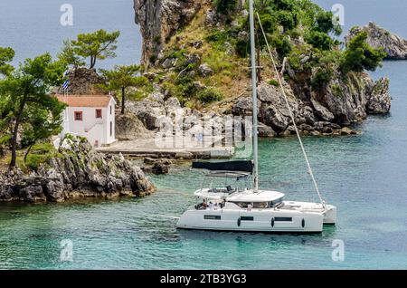 Weißes Segelboot schwimmt friedlich im Parga-Meer, Westgriechenland, neben einer kleinen üppigen grünen Insel mit einer Kapelle. Wunderschönes Türkisfarbenes Wasser Stockfoto