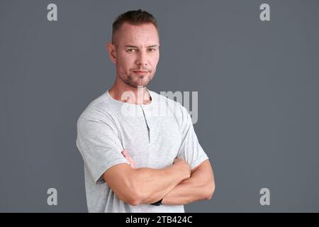 Porträt eines selbstbewussten reifen Mannes im grauen T-Shirt, der Arme kreuzt und in die Kamera blickt Stockfoto