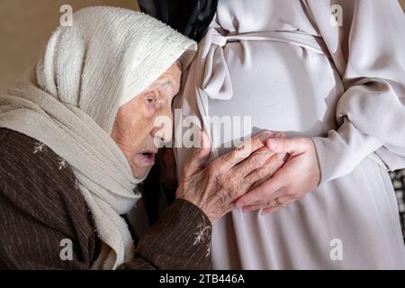 muslimische alte Frau, die sich für ihren neuen Enkel aufgeregt fühlt, berühre den Bauch ihrer Tochter, um Bewegungen des Fötus zu spüren Stockfoto
