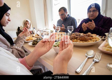 Familienessen mit Mitgliedern mehrerer Generationen im modernen Wohnzimmer, beten vor dem Essen im ramadan Stockfoto