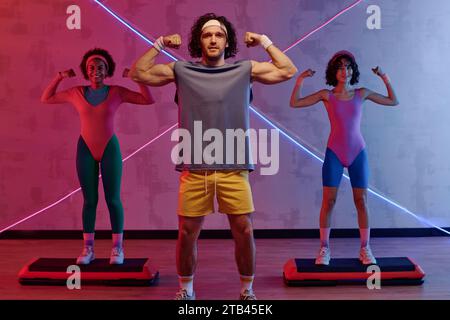 Junge kaukasische Athletin und zwei birassische Mädchen zeigen ihre Muskeln vor rosa blauem Hintergrund Stockfoto