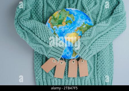 Ärmel aus Strickpullover umarmen den Planeten mit Tags. Kleidung für verantwortungsbewussten Konsum. Umweltfreundlichkeit und nachhaltige Mode. Stockfoto