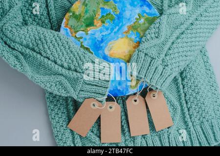 Ärmel aus Strickpullover umarmen den Planeten mit Tags. Kleidung für verantwortungsbewussten Konsum. Umweltfreundlichkeit und nachhaltige Mode. Stockfoto