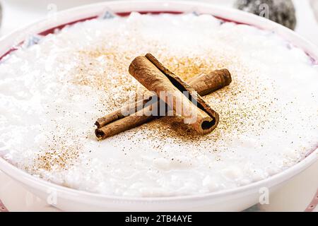 Reispudding-Schüssel, hausgemachter Pudding aus gemahlenem Reis, gesüßt mit Zimtpulver und Zimtrinde. Ländliche brasilianische Süßigkeiten im Hintergrund, Stockfoto