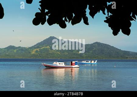 Fähre und Blick auf das Festland und Gunung Tumpa an einem östlichen Strand auf dieser Korallen gesäumten Urlaubsinsel. Bunaken Island, Nord-Sulawesi, Indonesien Stockfoto