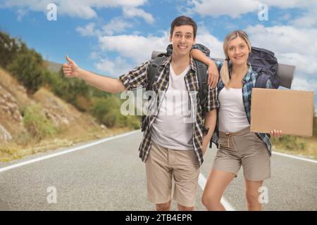 Ein paar Wanderer, die per Anhalter wandern und ein leeres Pappschild auf der Straße halten Stockfoto