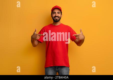 Selbstbewusster indischer Liefermann in roter Uniform und Mütze, der auf sich zeigt Stockfoto