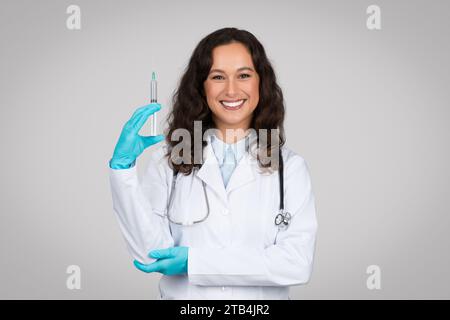 Fröhliche weiße Frau Ärztin trägt sterile Handschuhe, hält medizinische Spritze, vorbereitet für eine Injektion Stockfoto