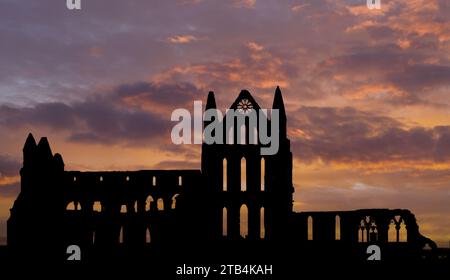 Whitby Abbey als Silhouette bei Sonnenuntergang mit Blick auf die Nordsee und den historischen Hafen in Whitby, North Yorkshire, England. Stockfoto