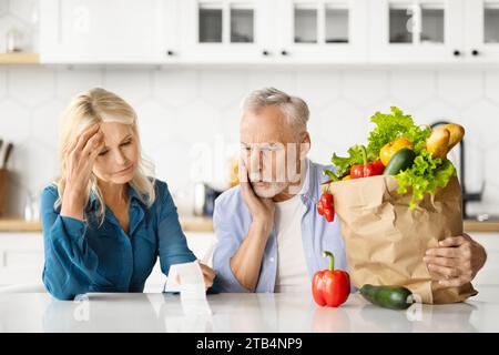 Besorgtes Seniorenpaar, das die Lebensmittelrechnung nach dem Einkaufen untersucht Stockfoto